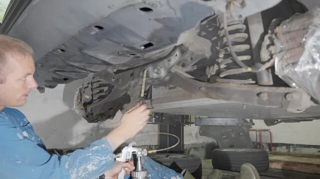Man sprays automotive lanolin product on car rear crossmember, wheel suspension and support components.