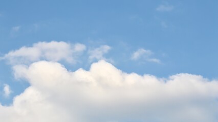 A serene sky background featuring a large, fluffy cumulus cloud that dominates the bottom frame, set against a soft and clear pale blue sky above, perfect for copy space.