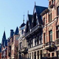 Historic European townhouses: one half-timbered style, the other red brick Neo-Renaissance, featuring intricate gables against a clear blue sky in Antwerp, Belgium