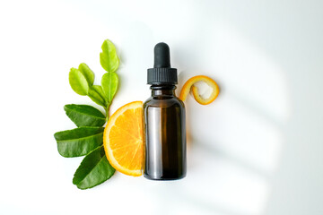 Amber glass dropper bottle with orange slice, citrus peel, and green leaves on white background. Perfect for beauty product advertisements, wellness, or natural cosmetic branding visuals