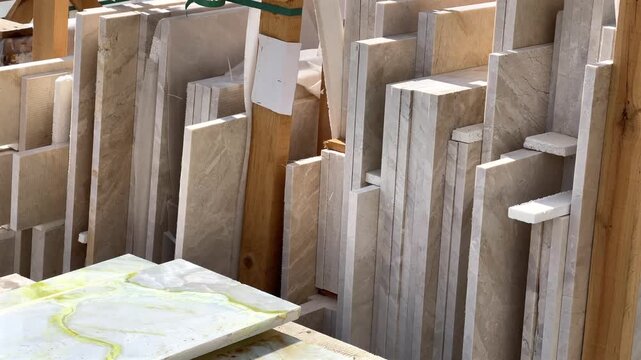 Various sizes and shades of beige and cream natural stone and marble slabs and tiles stacked vertically in a lumber rack at a construction supply or stone yard.