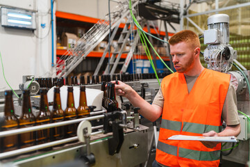 Man in safety vest inspecting bottles on a brewery production line, ensuring quality and overseeing manufacturing process