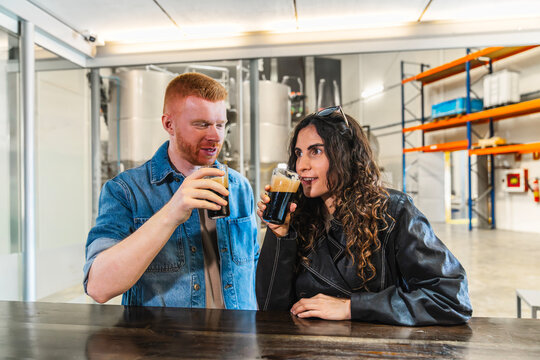 Happy couple enjoying dark craft beer samples at a brewery. Experiencing beer production and tasting flavor profiles