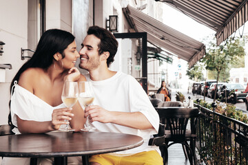 Smiling beautiful woman and her handsome boyfriend. Happy cheerful family. Sexy couple cheering with glasses of red wine at their date in restaurant. Drinking alcohol at veranda cafe