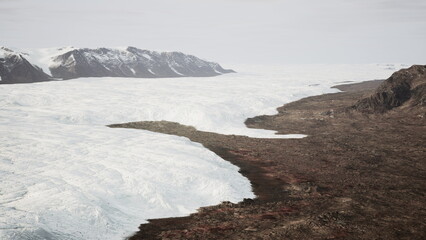 Towering glaciers stretch across the scene, merging with rugged terrain. The stark contrast of ice and earth creates a breathtaking view, highlighting natures beauty in a remote location.