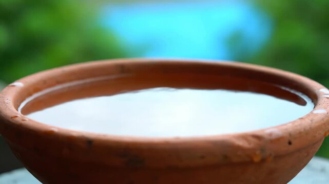 Water droplets falling into a terracotta bowl with ripples and then still water. Pseudoscientific concept to demonstrate liquid physics.