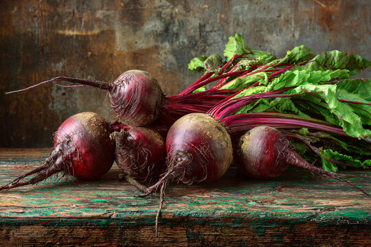 Freshly harvested vibrant red beets with green tops on rustic wooden table, healthy eating.