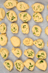 An overhead shot shows numerous unbaked dough rolls filled with Parmesan, garlic, and parsley, arranged on a baking sheet lined with parchment paper