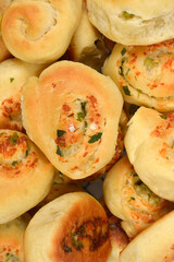 A macro overhead shot of a pile of freshly baked, soft parmesan, garlic, and parsley rolls, highlighting their golden-brown tops and savory filling