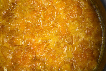 A close-up shows a thick, bubbling mass of bright orange mandarin marmalade being cooked in a metal pot, highlighting the chopped fruit pieces
