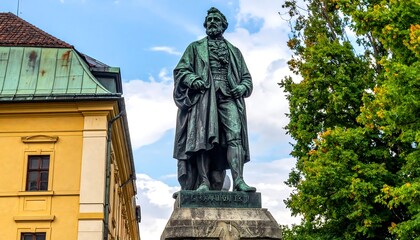 Obraz premium A bronze statue of a man stands prominently in a public square, framed by buildings and trees. Cloudy sky visible