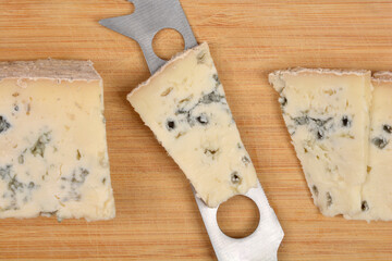 A close-up, top-down view shows slices of Gorgonzola blue cheese and a cheese knife on a wooden background
