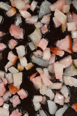 A close-up view shows small, diced pieces of bacon or pancetta, with both white fat and pink meat, frying in rendered fat on a dark surface