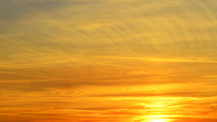 Sunset sky background with orange and yellow colors. Beautiful sunset. Aircraft contrail.