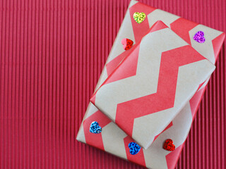 Top view of two gift boxes wrapped in red zigzag kraft paper with small flowers on red corrugated paper background. Concept for happy birthday, thank you, mother's day, anniversary, Valentine's day.
