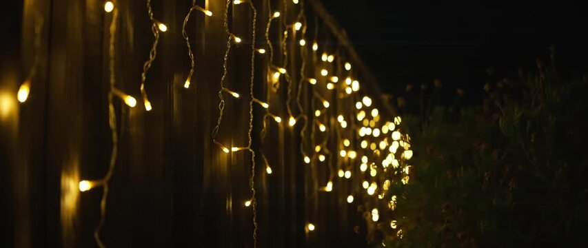 Warm glowing string lights hanging on wooden fence at night
