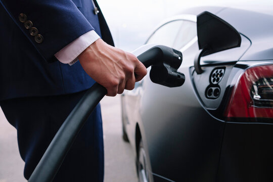 Hand of businessman holding power cable of electric car