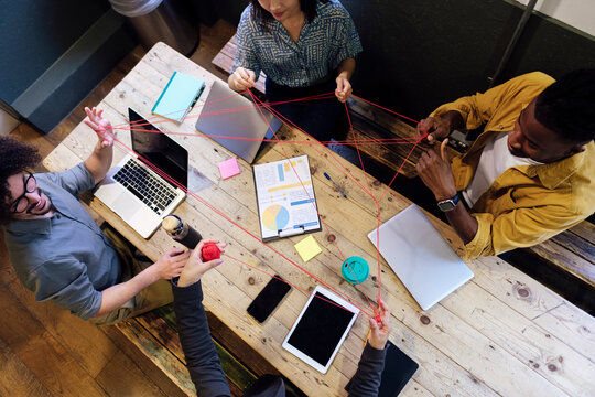 Business colleagues playing cat's cradle sitting at desk in office
