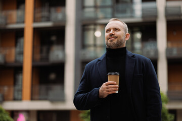 Smiling man in elegant coat holding coffee to go on street