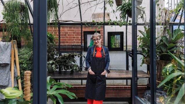 Mature garden owner with hands in pockets at greenhouse