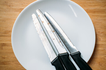 Close-up of three rusty kitchen knives with black handles resting on a white plate. Sustainable...