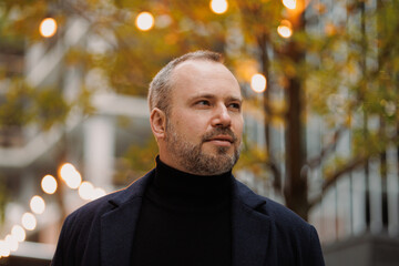 Portrait of elegant man in coat looking away on city street in autumn