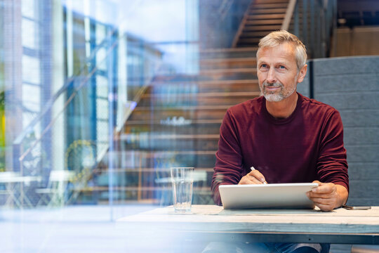 Thoughtful man using a tablet at modern office desk