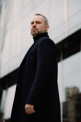 Businessman in coat looking at camera near office building on street