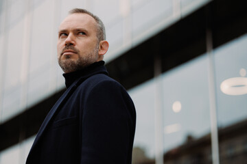 Portrait of businessman in autumn coat looking away near office building on street