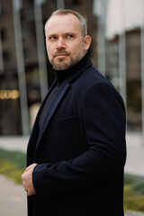 Portrait of adult man in turtleneck and coat looking away on city street