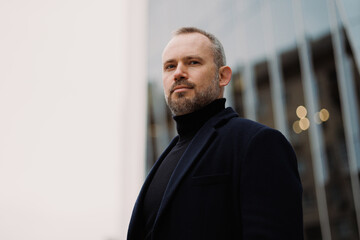 Adult man in elegant coat looking at camera on city street