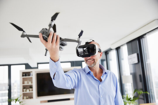 Entrepreneur wearing virtual reality headset holding quadcopter while standing at home