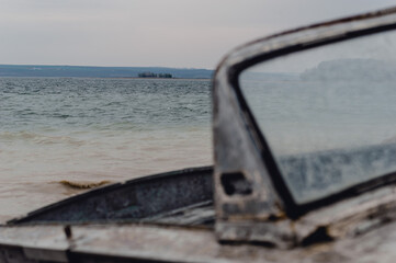 A weathered boat side mirror overlooking a calm lake with distant shoreline and overcast sky