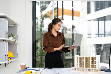 Young female engineer designer or contractor working on drawing plans analyzing structure on laptop computor at construction site office. copy space.