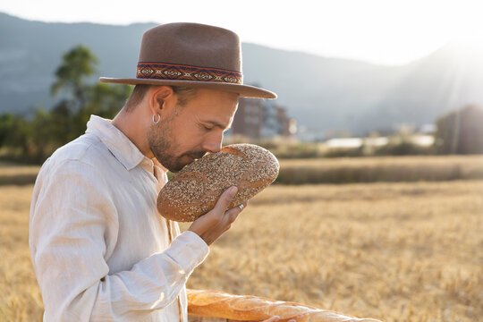 Person smelling bread in wheat field at golden hour during summer harvest
