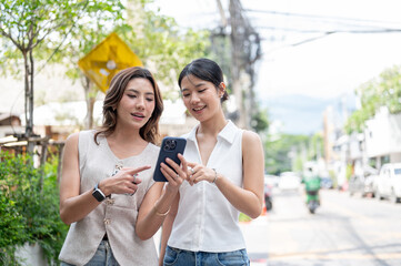 Asian woman holding phone checking map or calling taxi car while standing with friend by street road