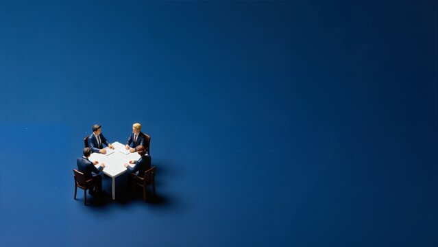 Two individuals seated at a round table against a deep blue background, viewed from above