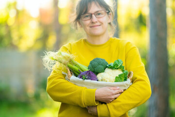 Portrait of woman farmer smiling with basket of broccoli, cauliflower, kohlrabi and corn. Autumn...