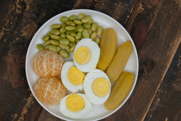 A plate of healthy breakfast. Balance diet. Boiled egg, steamed banana, boiled edamame, tangerine.
