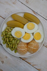 A plate of healthy breakfast. Balance diet. Boiled egg, steamed banana, boiled edamame, tangerine.
