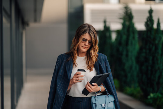 Businesswoman walking and using digital tablet while holding coffee