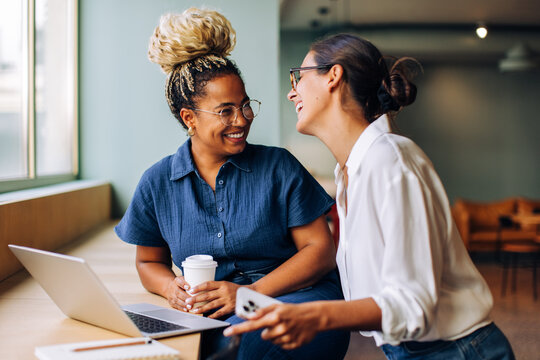 Fototapeta Two women enjoying a cheerful conversation by a laptop