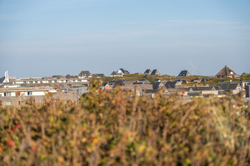 A panoramic view of coastal houses spread across gentle dunes under a clear sky. The mixture of modern and traditional roofs defines the seaside village charm.