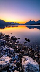 Sunset lake scene; rocks on shore, mountains reflected