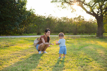 Fototapeta premium Mother holding baby son walking together at sunny park