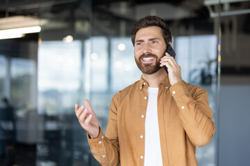 Smiling professional man on a phone call in a bright open-plan office, confidently managing business communication and networking while staying connected and productive