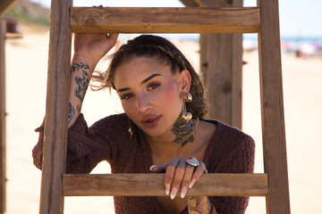 A beautiful young woman in a brown dress rests her arms on the steps of the wooden ladder of the lifeguard hut on the beach. The woman is sad and depressed and is going through a difficult time.