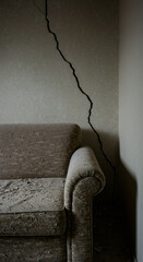 Dust covered sofa below large crack on damaged wall. Desolate interior of an abandoned home after natural disaster. Earthquake destruction.