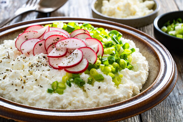 Cottage cheese with scallions and radishes on wooden table