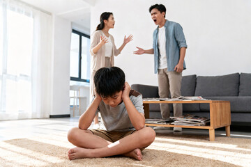 Sad boy sitting on carpet covering ears, parents arguing behind him, emotional distress, psychological impact, need for support, child mental health, tense family situation